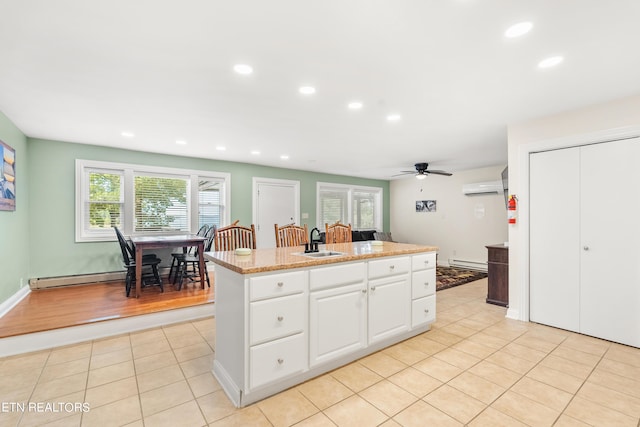 kitchen with a sink, a ceiling fan, a wall unit AC, baseboard heating, and light tile patterned floors