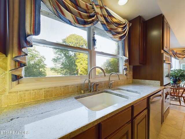 kitchen featuring stainless steel dishwasher, sink, light stone countertops, and light tile patterned floors