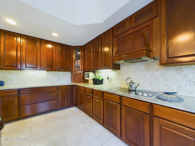 kitchen featuring custom range hood, light stone countertops, decorative backsplash, and stovetop