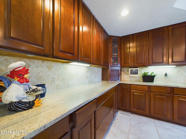 kitchen featuring decorative backsplash, light stone counters, a textured ceiling, and light tile patterned floors