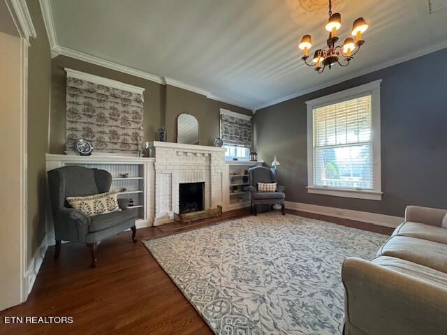 living room featuring ornamental molding, hardwood / wood-style floors, a brick fireplace, and an inviting chandelier