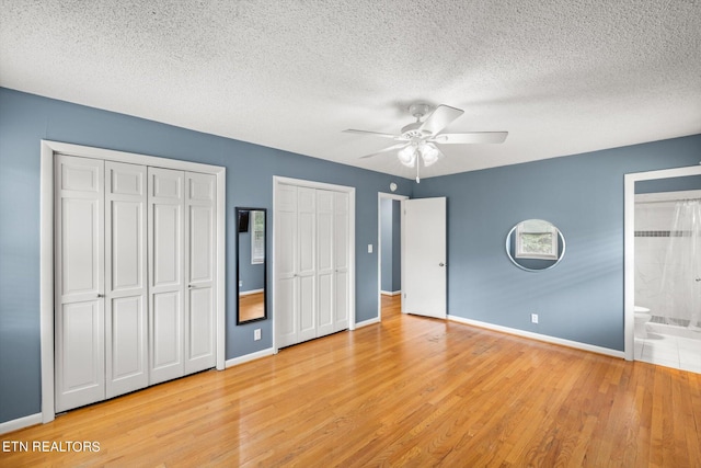 unfurnished bedroom featuring two closets, ensuite bathroom, light wood-type flooring, ceiling fan, and a textured ceiling