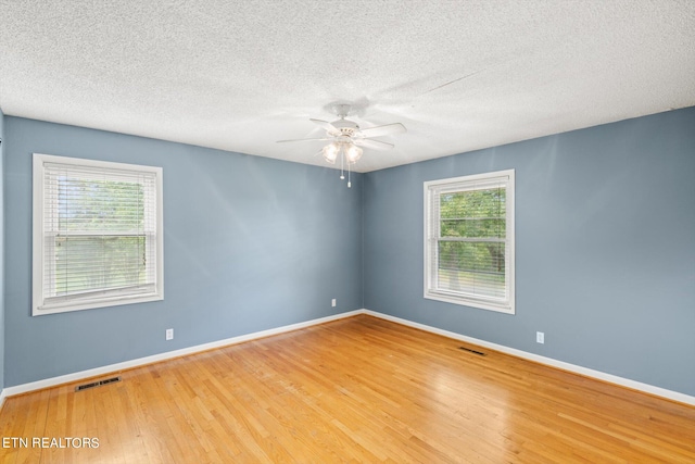 unfurnished room with ceiling fan, a wealth of natural light, wood-type flooring, and a textured ceiling