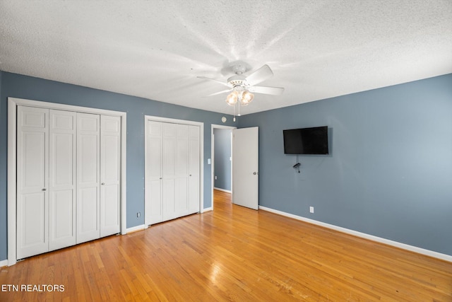 unfurnished bedroom featuring two closets, ceiling fan, a textured ceiling, and light hardwood / wood-style flooring