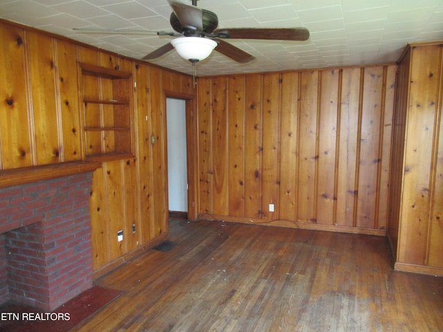 10827 Rutledge Pike, Blaine, TN 37709 - unfurnished living room featuring a brick fireplace, baseboards, ceiling fan, wood walls, and hardwood / wood-style flooring