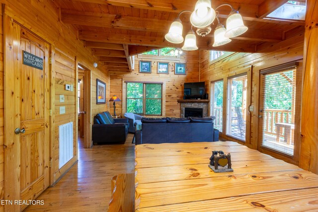 dining space with wood walls, wooden ceiling, a fireplace, light hardwood / wood-style flooring, and beam ceiling