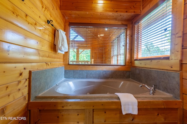 bathroom with plenty of natural light, wooden walls, and a relaxing tiled tub