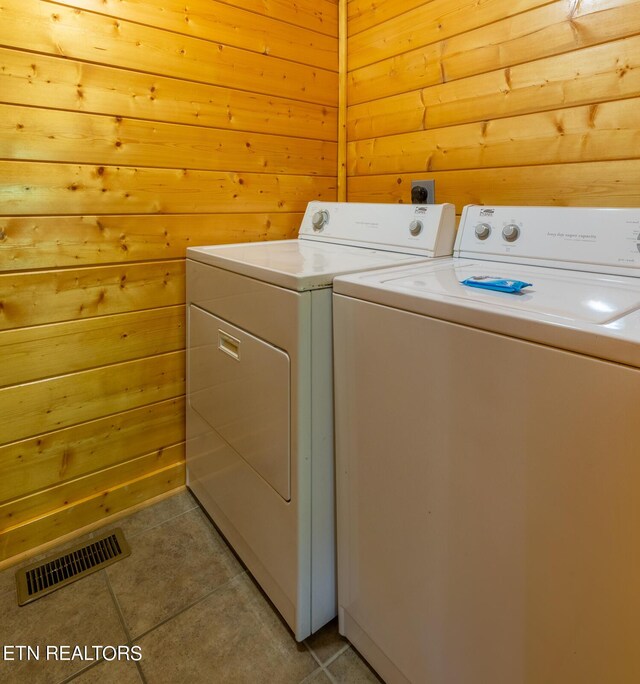 clothes washing area featuring wood walls, light tile patterned floors, and washing machine and clothes dryer