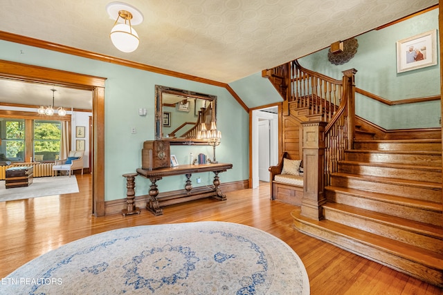 stairway featuring ornamental molding, a textured ceiling, wood-type flooring, and an inviting chandelier