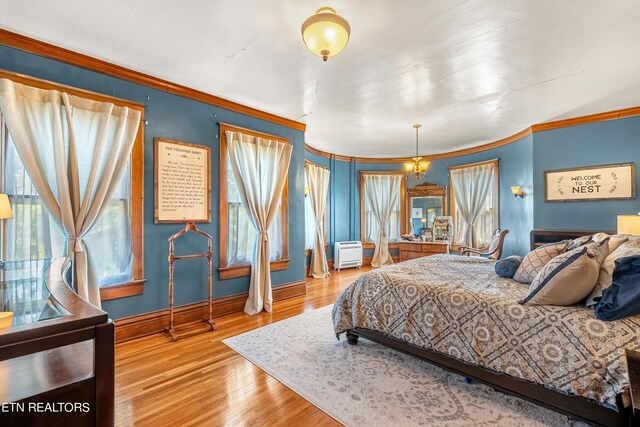 bedroom with ornamental molding, wood-type flooring, and a chandelier