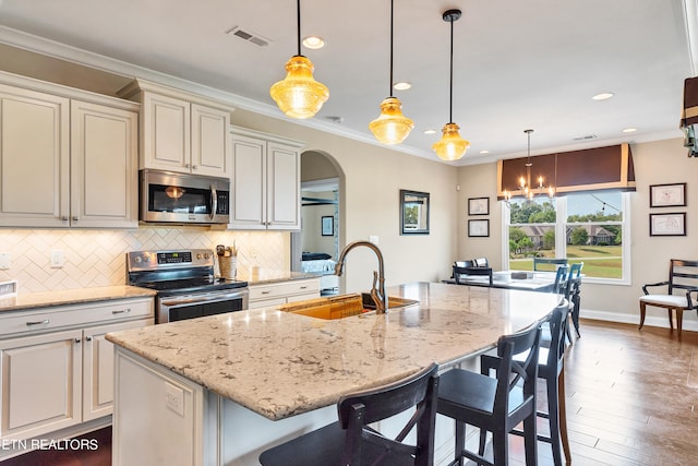 kitchen with pendant lighting, an island with sink, sink, light stone countertops, and appliances with stainless steel finishes