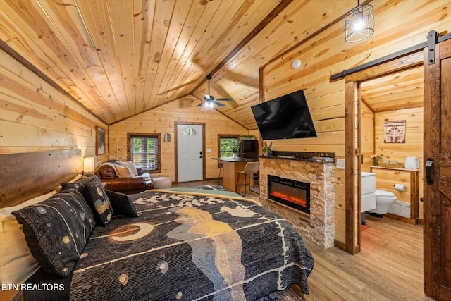 bedroom featuring wooden walls, light hardwood / wood-style flooring, lofted ceiling with beams, a fireplace, and a barn door