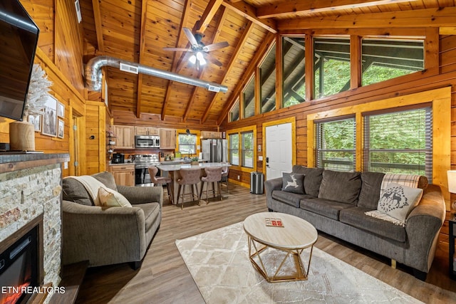 living room with ceiling fan, wood ceiling, a stone fireplace, wooden walls, and light wood-type flooring