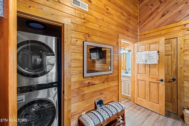 washroom featuring wood walls, light hardwood / wood-style floors, and stacked washer / dryer