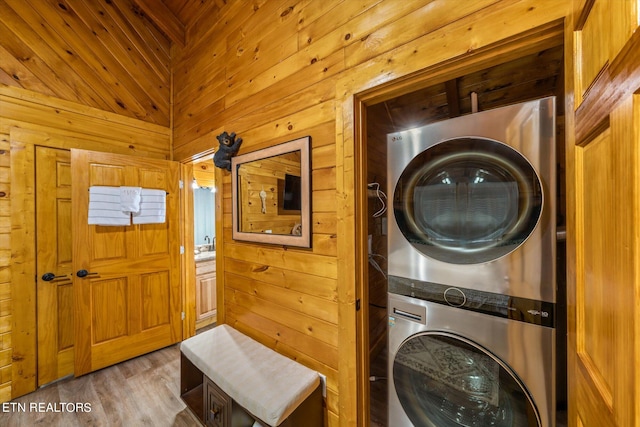 laundry area with wooden walls, stacked washer / dryer, and hardwood / wood-style flooring