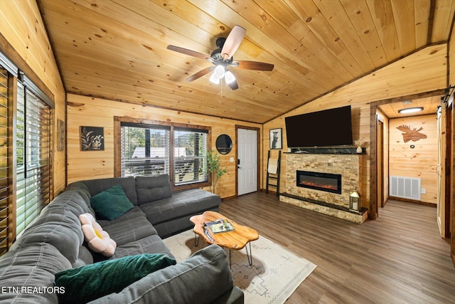 living room featuring ceiling fan, wood walls, wood-type flooring, a stone fireplace, and wooden ceiling