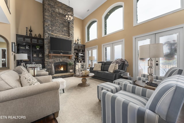 living room with french doors, a high ceiling, a stone fireplace, crown molding, and wood-type flooring