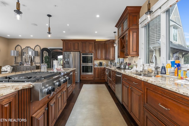 kitchen with light stone countertops, appliances with stainless steel finishes, decorative light fixtures, and sink