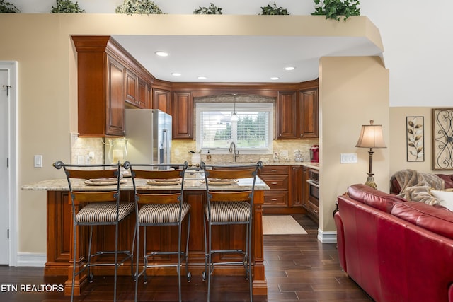 kitchen featuring backsplash, dark wood-type flooring, appliances with stainless steel finishes, and a breakfast bar area