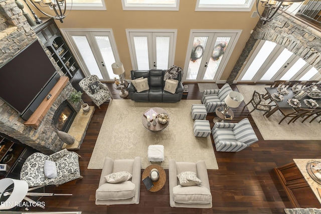 living room with a chandelier, a stone fireplace, a high ceiling, and french doors