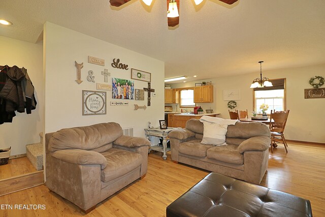 living room with sink, ceiling fan with notable chandelier, light hardwood / wood-style floors, and a textured ceiling