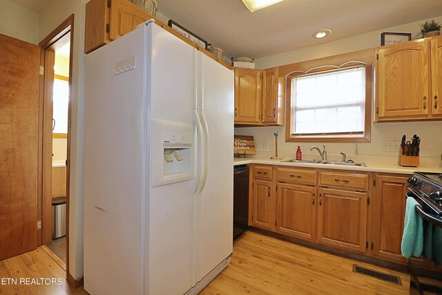 kitchen with white refrigerator with ice dispenser, a textured ceiling, light hardwood / wood-style flooring, gas stove, and sink