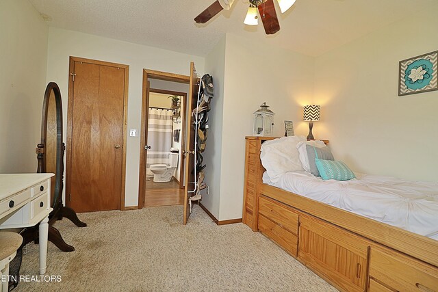 bedroom with ceiling fan, ensuite bathroom, light carpet, and a textured ceiling