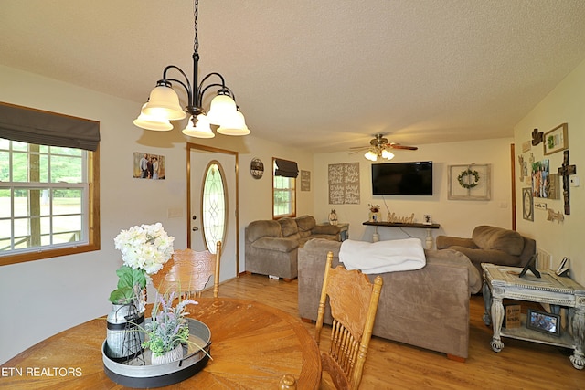 dining area with a textured ceiling, light wood-style floors, and ceiling fan with notable chandelier