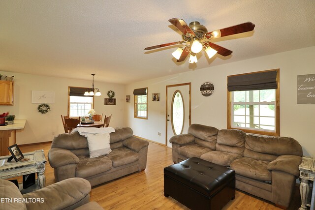 living room with light wood-type flooring, ceiling fan with notable chandelier, and a textured ceiling