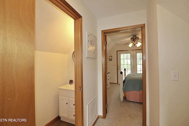hall with baseboards, carpet floors, a textured ceiling, and visible vents
