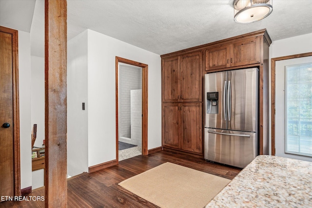 kitchen featuring stainless steel fridge, light stone counters, dark hardwood / wood-style flooring, and a textured ceiling