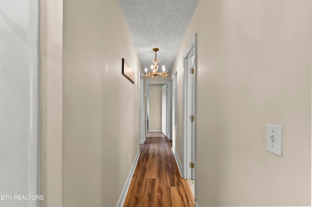 corridor featuring a textured ceiling, an inviting chandelier, and dark wood-type flooring