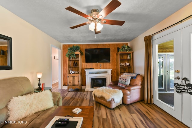 living room featuring ceiling fan, wood-type flooring, a textured ceiling, and wooden walls