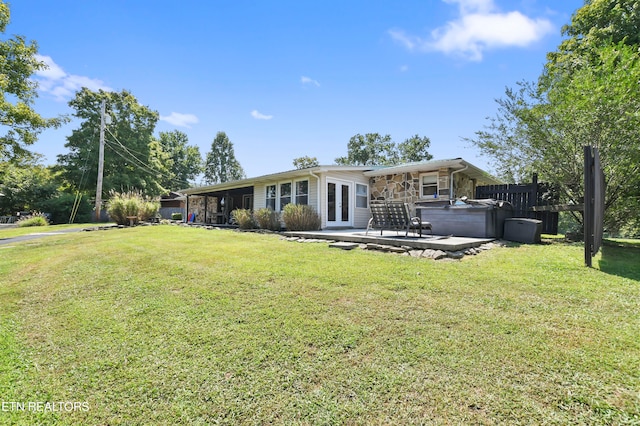 back of property with a lawn, a patio area, and a hot tub