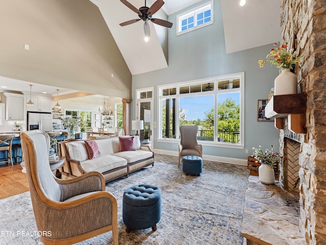 living room with high vaulted ceiling, a stone fireplace, ceiling fan, and light hardwood / wood-style floors