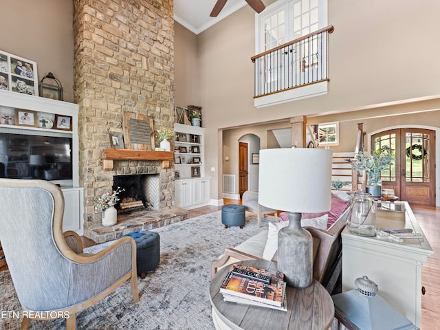 living room with a high ceiling, a fireplace, wood-type flooring, crown molding, and ceiling fan