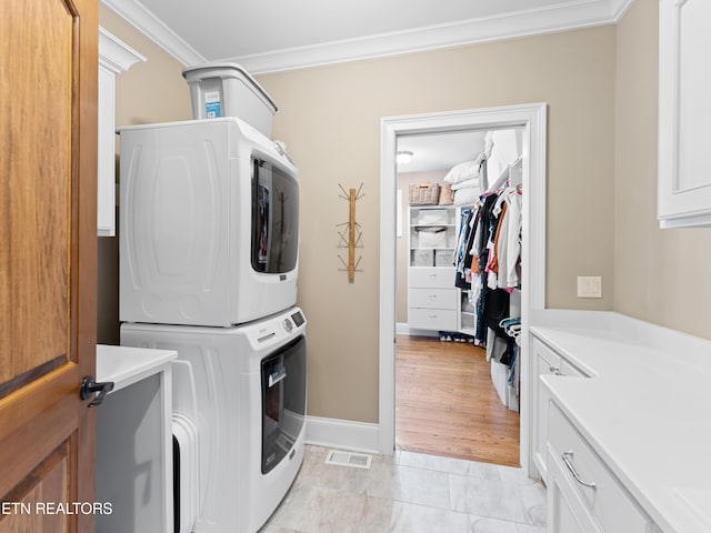 laundry area with light wood-type flooring, cabinets, stacked washer and clothes dryer, and crown molding