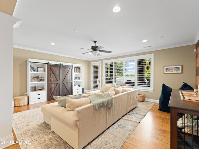 living room with crown molding, a barn door, ceiling fan, and light wood-type flooring