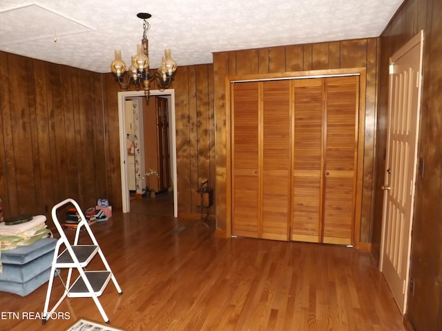 unfurnished dining area with hardwood / wood-style floors, a textured ceiling, a notable chandelier, and wood walls