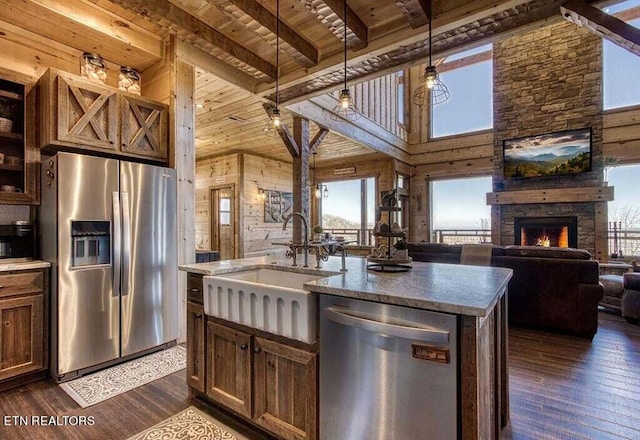 kitchen with wood ceiling, an island with sink, a stone fireplace, dark hardwood / wood-style floors, and appliances with stainless steel finishes