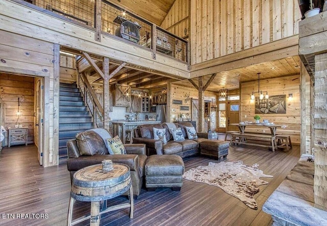 living room with dark hardwood / wood-style flooring, high vaulted ceiling, a chandelier, and wood walls