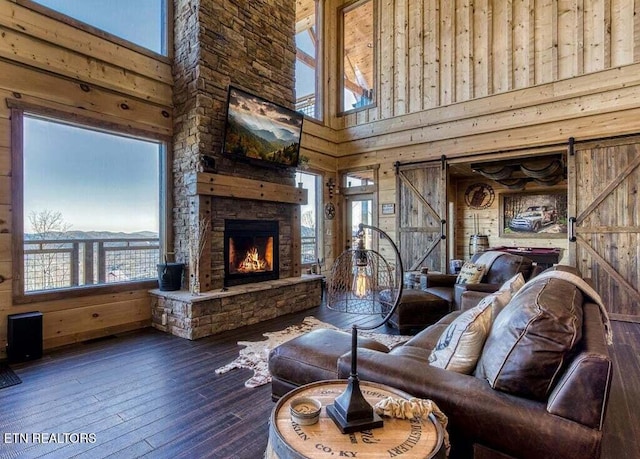 living room featuring a fireplace, hardwood / wood-style floors, a high ceiling, wooden walls, and a barn door