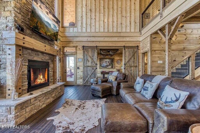 living room featuring dark hardwood / wood-style flooring, wooden walls, a high ceiling, and a stone fireplace