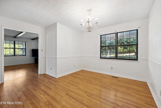 empty room with a textured ceiling, light hardwood / wood-style flooring, and a notable chandelier