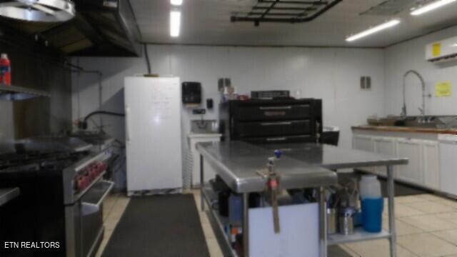 kitchen with stainless steel range with gas stovetop, white cabinetry, sink, white fridge, and an AC wall unit