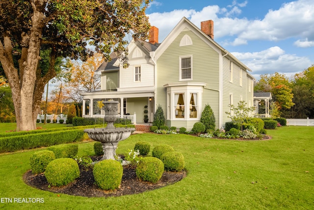 rear view of property with a yard, a porch, a chimney, and fence