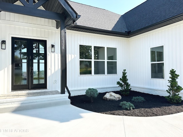 view of exterior entry featuring french doors, a shingled roof, and board and batten siding