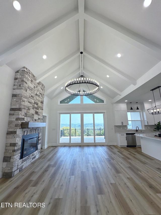 unfurnished living room with beam ceiling, a notable chandelier, light wood-style flooring, a stone fireplace, and high vaulted ceiling