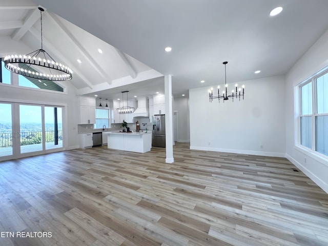 unfurnished living room with an inviting chandelier, light wood finished floors, a wealth of natural light, and beamed ceiling