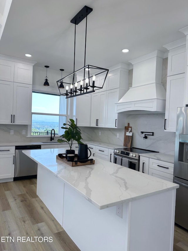 kitchen featuring custom range hood, decorative backsplash, appliances with stainless steel finishes, white cabinets, and a kitchen island